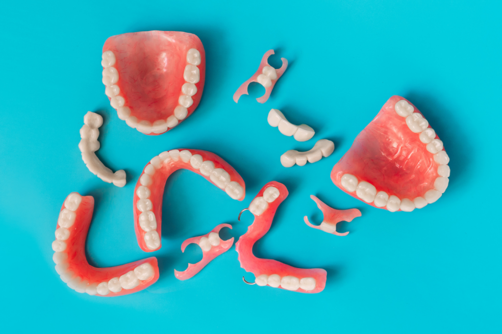 Top view of a set of dentures on a blue background, including a full denture, a partial denture, and an overdenture.