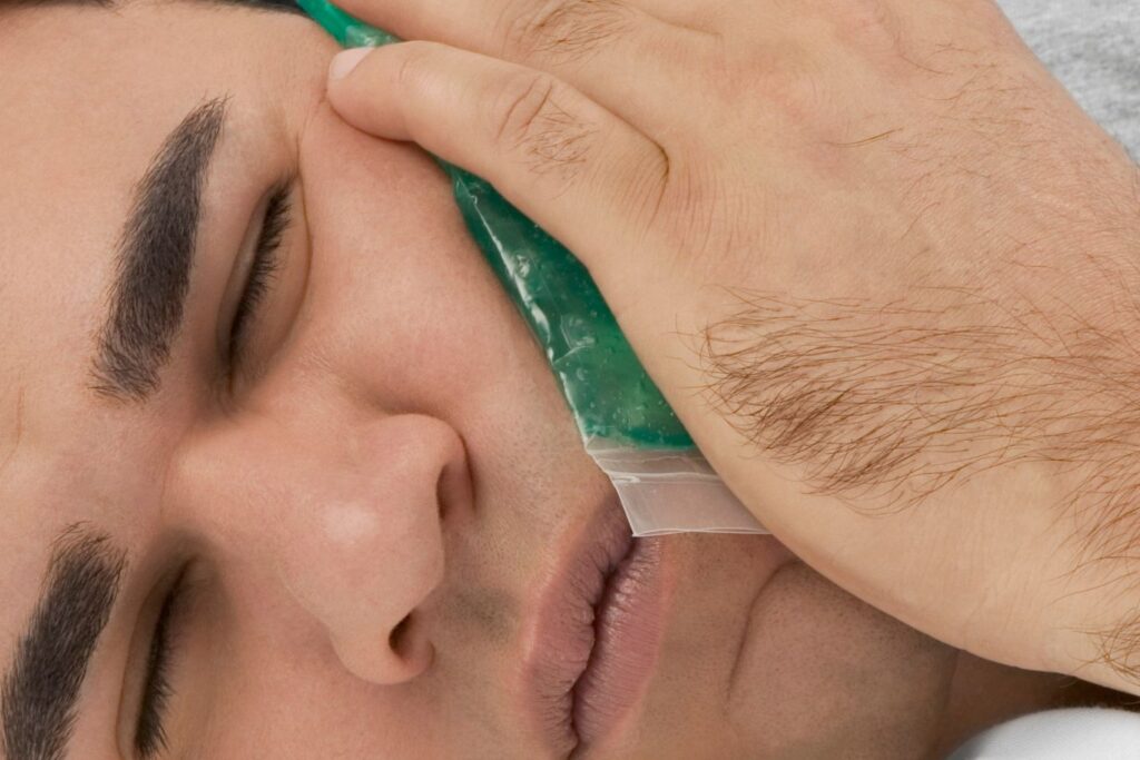 A young man applying an ice pack to his cheek to manage post-procedure dental pain or swelling
